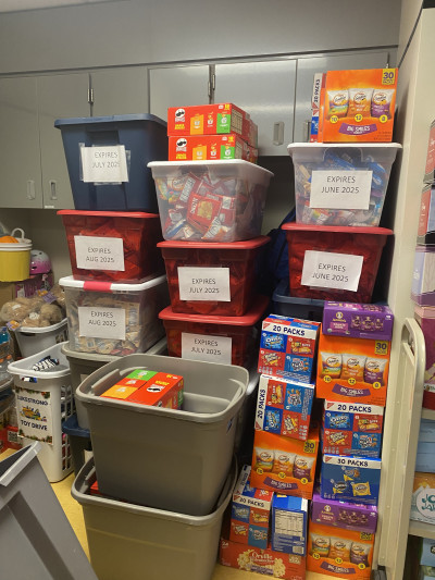 Boxes of snacks like crackers and cookies are stacked along with additional snacks labeled in bins.